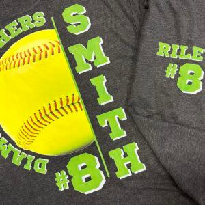 A grey softball jersey printed with a player name, number and a large softball graphic
