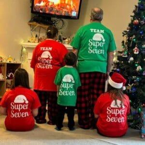 A family photographed from behind in matching red and green Team Super Seven Christmas shirts