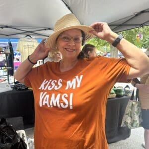 A customer at an outdoor market stall wearing an orange Kiss My Yams tee