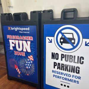 Two A-frame pavement signs, one for a Firecracker Fun Zone and one reserving parking for performers