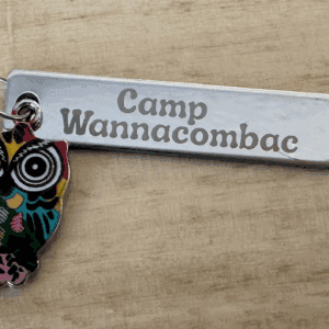 An engraved metal Camp Wannacombac keyring hung with a colourful owl charm