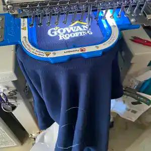 A navy Gowan Roofing polo hooped in the embroidery machine as the logo stitches out
