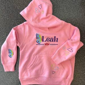 A child's pink hoodie with an embroidered name and heart appliqués on the hood and sleeves
