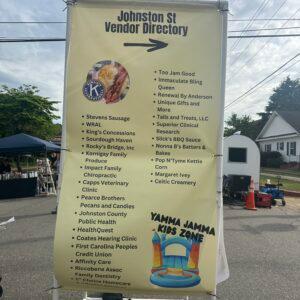 A tall printed vendor directory banner listing stallholders at an outdoor street event