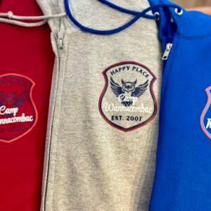Camp Wannacombac hoodies in red, grey and blue, each with a printed winged crest