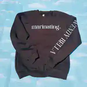 A black crewneck sweatshirt printed with the word marinating, and lettering down one sleeve
