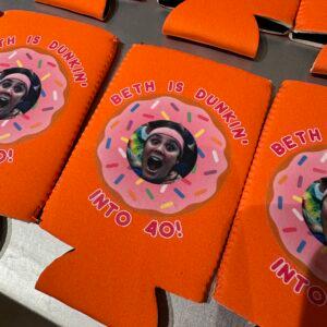 Printed can coolers laid out in rows, each with the same doughnut birthday design