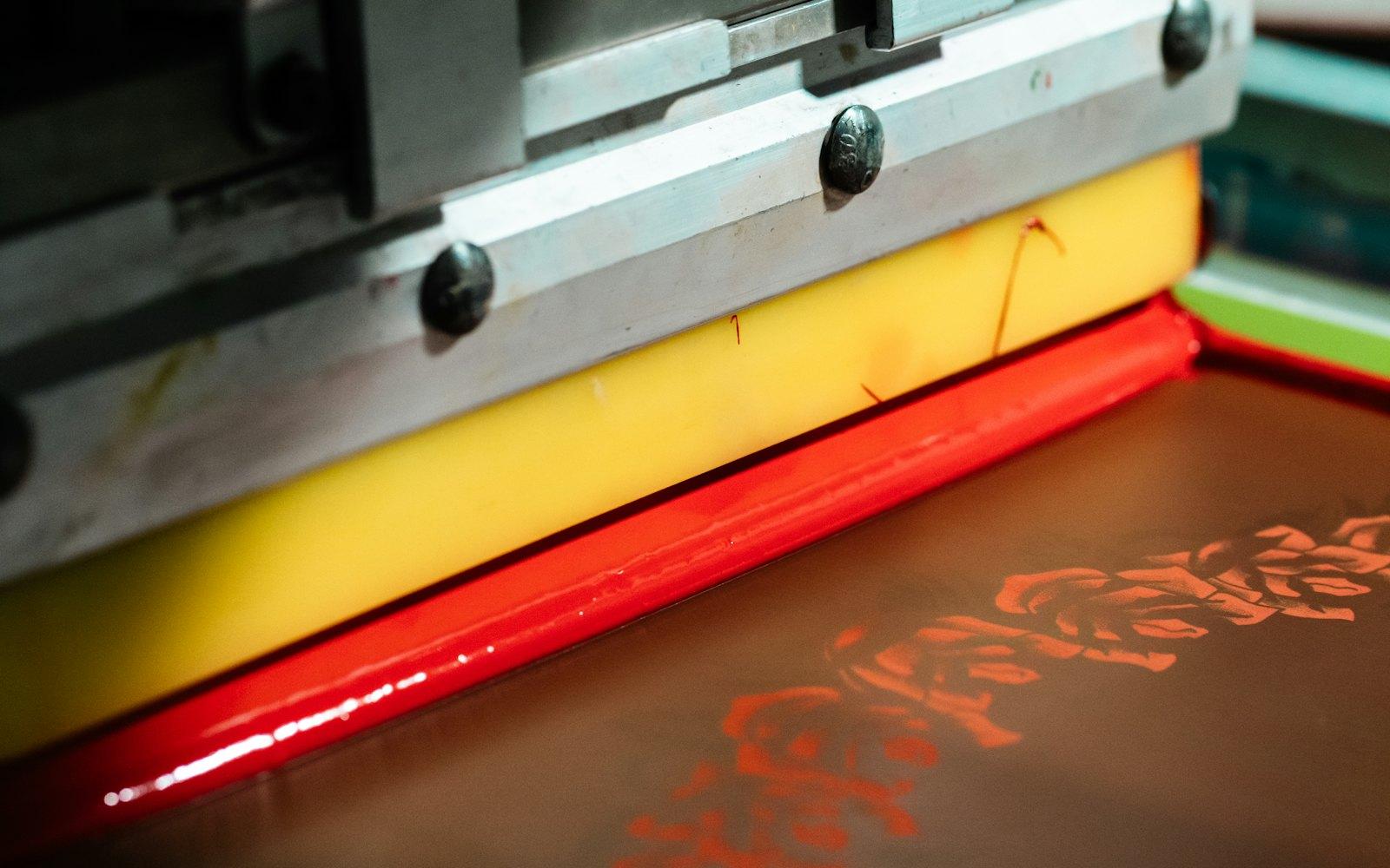 A screen printing press pulling red ink across a screen